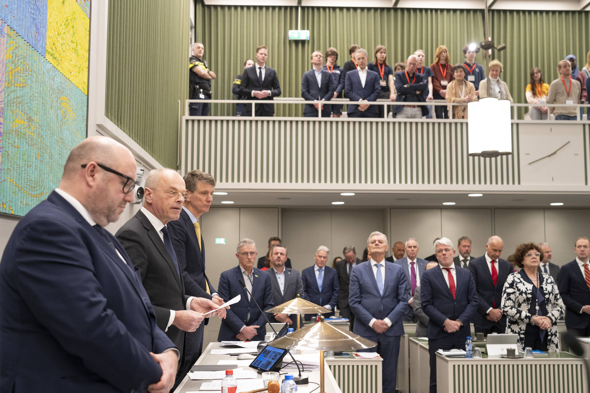 Foto van een volle vergaderzaal van de Eerste Kamer. Alle aanwezigen staan. Aan de linkerkant spreekt een persoon.