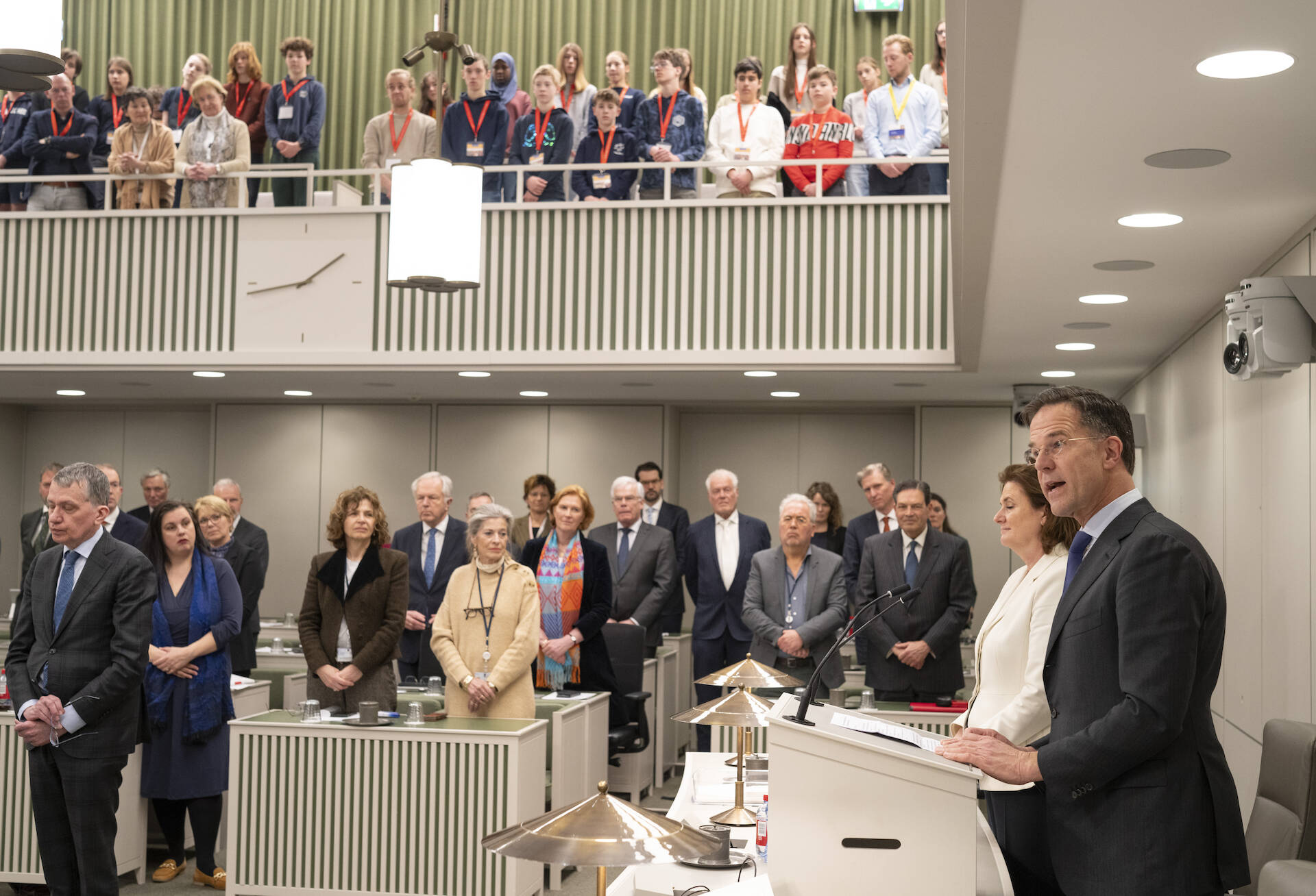 Foto van een volle vergaderzaal van de Eerste Kamer. Alle aanwezigen staan. Aan de rechterkant spreekt een persoon.