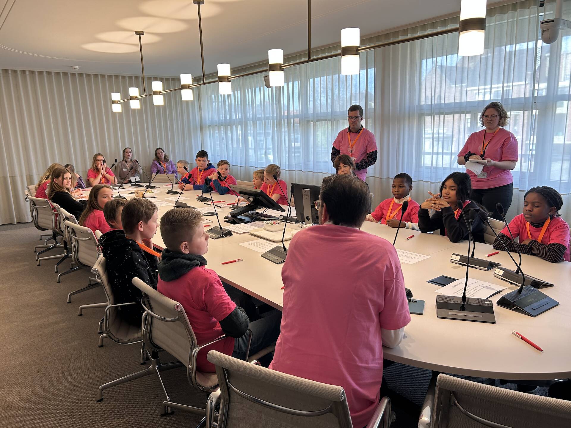Een groep kinderen in roze t-shirts aan een vergadertafel