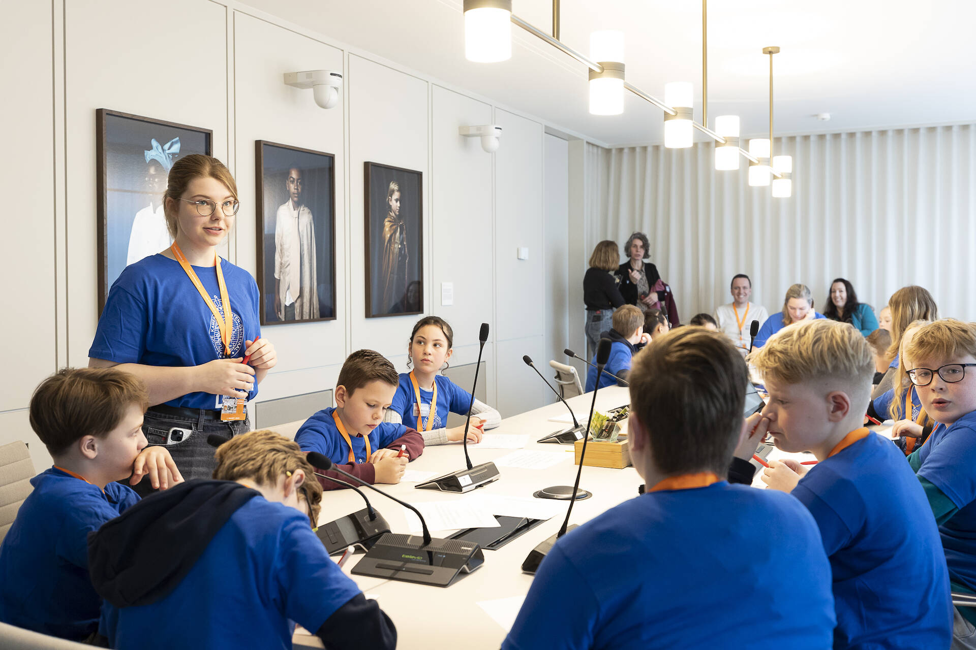 Een groep kinderen in blauwe t-shirts aan een vergadertafel