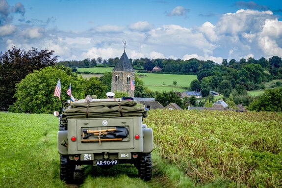 Een legervoertuig met daarin veteranen en het koningspaar rijdt de grens over van België naar Nederland