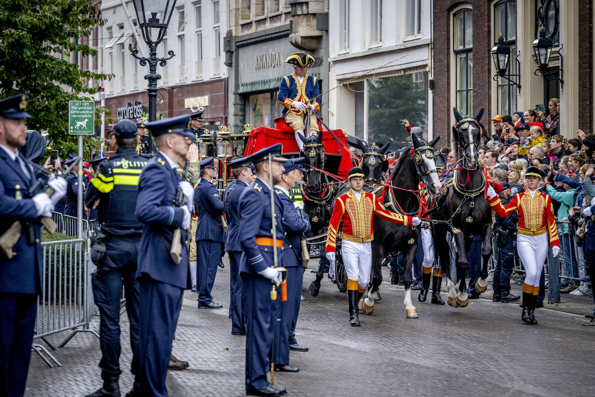 De Glazen Koets rijdt door de straten van Den Haag. Toeschouwers staan te kijken en te zwaaien naar leden van het Koninklijk Huis.