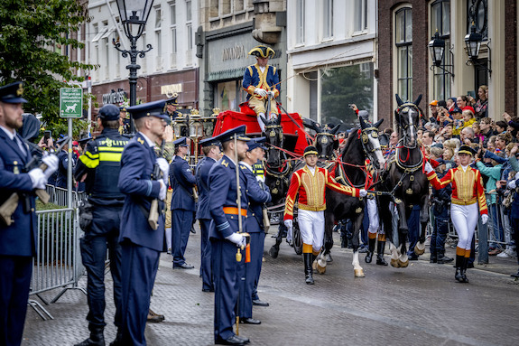 De Glazen Koets rijdt door de straten van Den Haag. Toeschouwers staan te kijken en te zwaaien naar leden van het Koninklijk Huis.