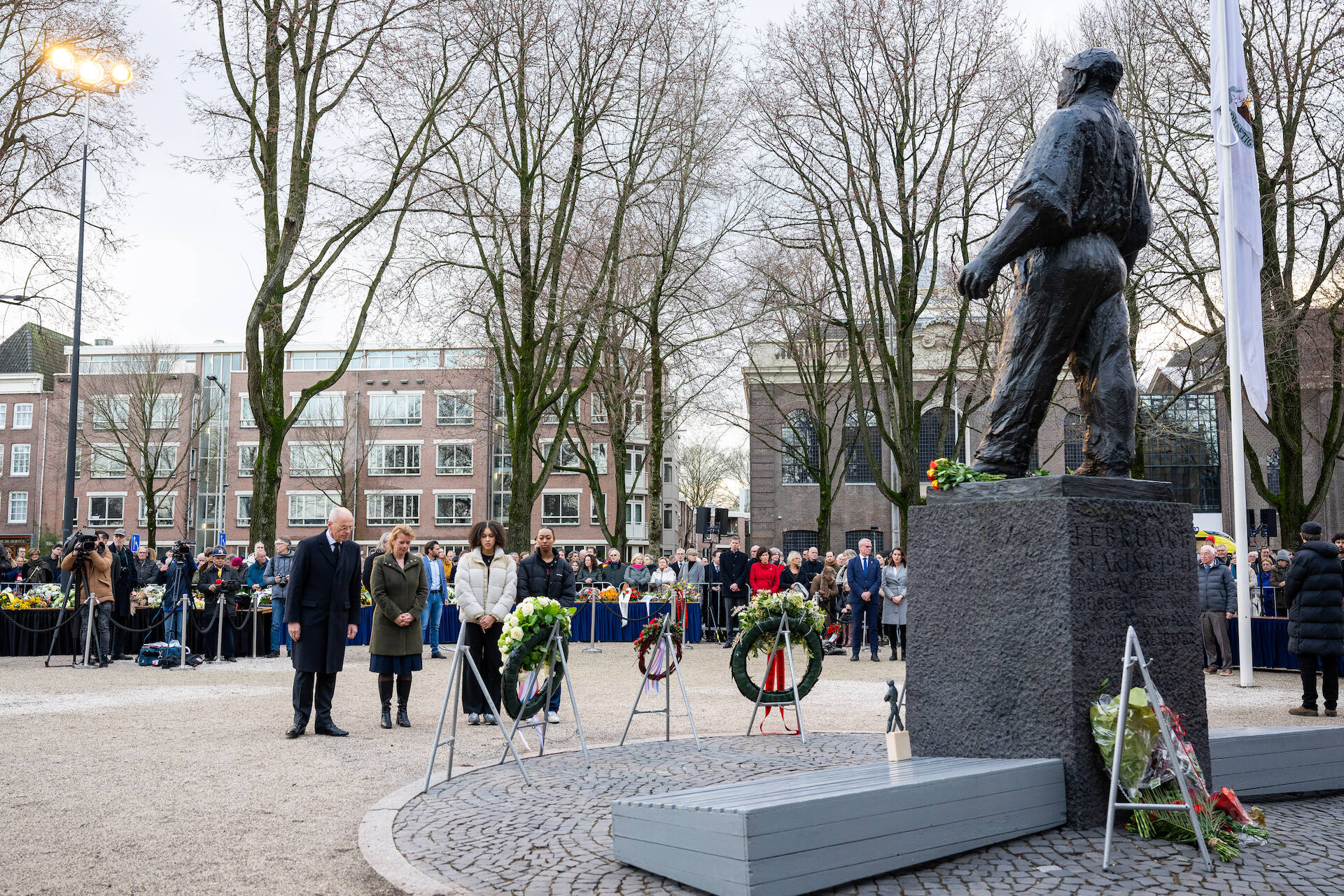 Mensen rondom een standbeeld van een dokwerker op de voorgrond. In het midden een man en een vrouw die voor een standaard met een krans staan.