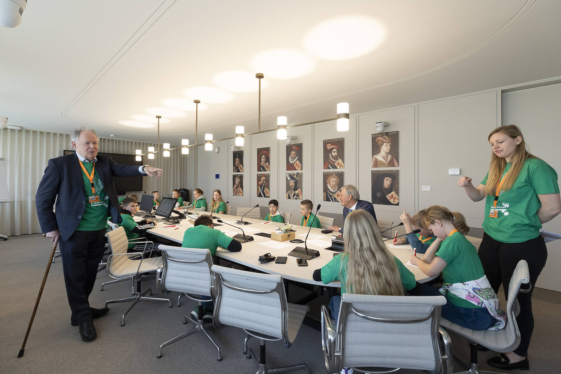 Een groep kinderen in groene t-shirts aan een vergadertafel